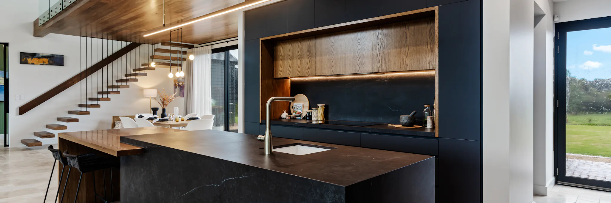 Black panelled kitchen with timber veneer feature doors for upper cabinets and underneath lighting. A black island with a drop down to a timber veneer benchtop